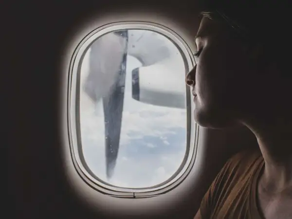 Frau blickt aus dem Flugzeugfenster, während das Flugzeug turbulenzen extrem durchfliegt. Wolken und ein Propeller sind sichtbar.
