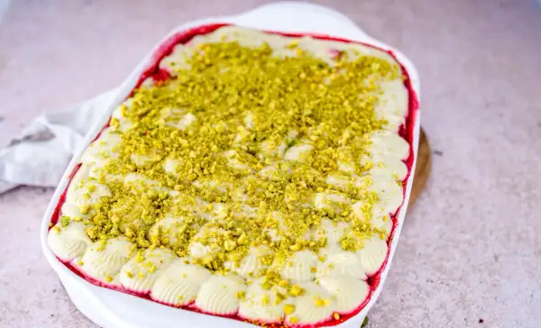 Ein cremiges Pistazien Tiramisu in einer weißen Auflaufform, bestreut mit gehackten Pistazien.