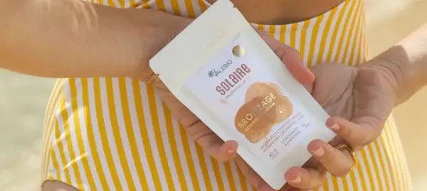 Une main tient un paquet de "Solaire Bronzage" de Valebio, suggérant une peau protégée et hâlée.