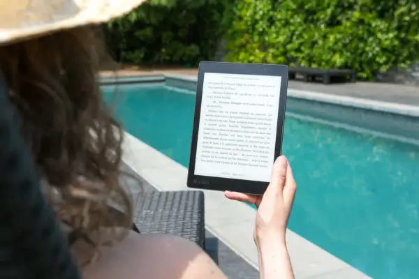 Une personne lit un epub en ligne au bord d'une piscine, profitant du soleil et d'une lecture immersive.