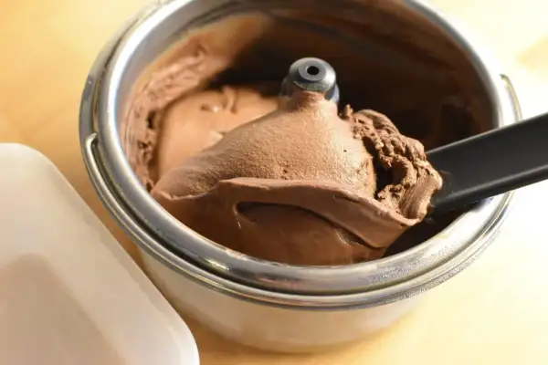 Un cucchiaio nero preleva una porzione di cremoso gelato fatto in casa al cioccolato da una gelatiera.