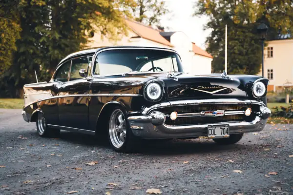Svart Chevrolet Bel Air bil från 1957 parkerad på grusväg med höstlöv.