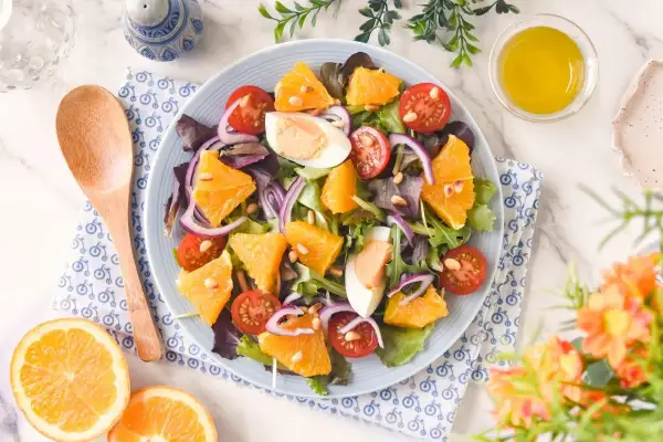 Ensalada de naranja vibrante con tomates cherry, huevo duro, cebolla morada y piñones. Una delicia fresca y colorida.
