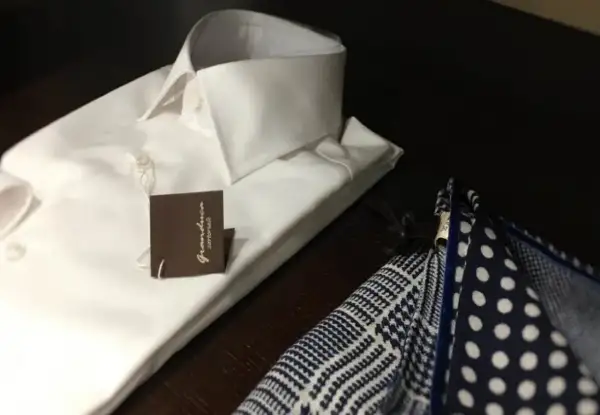 Camicia bianca da uomo con abbottonatura maschile impeccabile, accanto a un fazzoletto da taschino a pois e a quadretti.