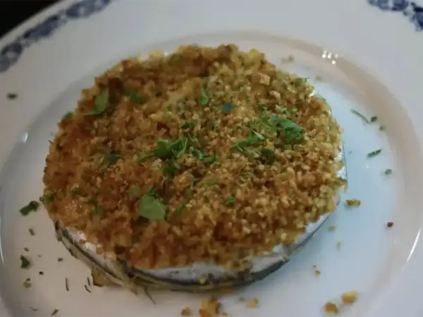 Tortino di alici dorato e croccante, guarnito con prezzemolo fresco, servito su un piatto bianco con bordo blu.