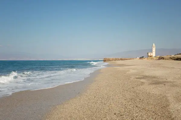 La Fabriquilla, Almería. Una playa de guijarros con el mar azul y una torre blanca solitaria.