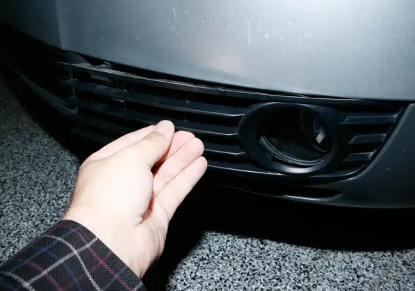 Dłoń naciska na kratkę zderzaka Audi A6 C5, obok otworu na światło przeciwmgielne.