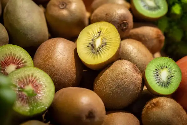 Ein Haufen Kiwis, einige ganz, andere aufgeschnitten, zeigen ihr grünes und gelbes Fruchtfleisch. Perfekt für einen gesunden Snack vor dem Schlafen.
