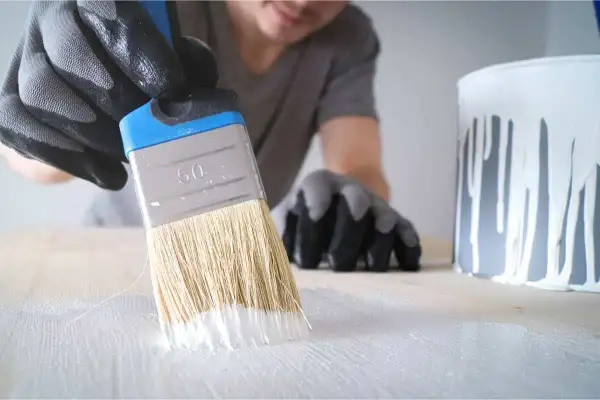 Mano guantata stende cementite bianca su una superficie di legno con un pennello.