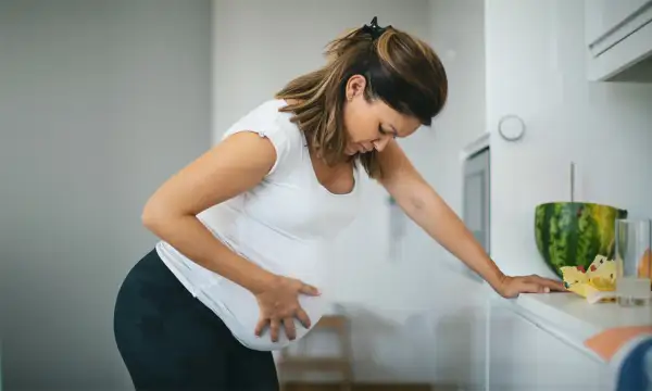 Schwangere Frau mit Hand auf dem Bauch, die sich vorbeugt. Sie fragt sich, ab wann Vorwehen auftreten können.