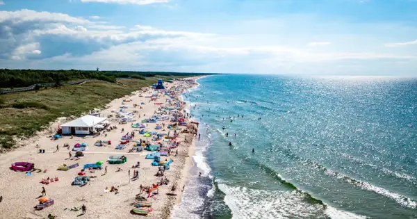 Słoneczna plaża w Darłowie tętni życiem. Tłumy plażowiczów, kolorowe parawany i namioty, a w wodzie kąpielowicze i surferzy. To idealne miejsce na wakacyjne atrakcje.