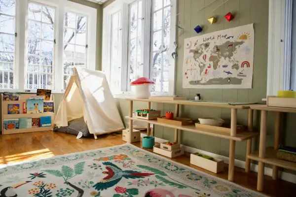A child's playroom set up with the Montessori method at home, featuring a tent, world map, and wooden shelves with educational toys and books.