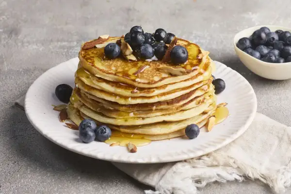 Stapel goldbrauner Pancakes, garniert mit Blaubeeren, Mandelsplittern und Honig. Ein köstliches Rezept für High Protein Pancakes.