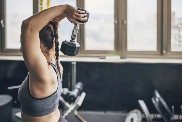 Kvinna utför tricep press med en hantel i gymmet.