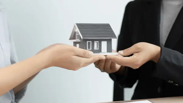 Manos intercambian una maqueta de casa, simbolizando la gestión de alquileres y la transferencia de propiedades.
