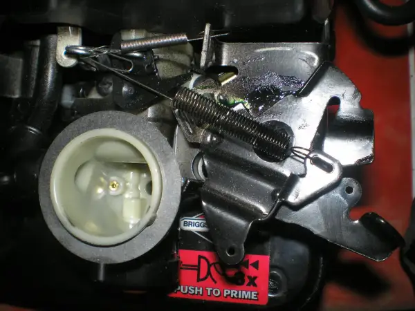 Mechanizm kosiarki z widoczną linką gazu, sprężynami i elementami gaźnika.