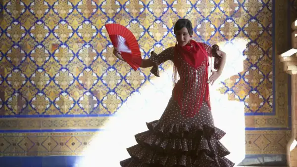Tancerka w hiszpańskim stroju flamenco, z wachlarzem w dłoni, na tle zdobionej kafelkami ściany.