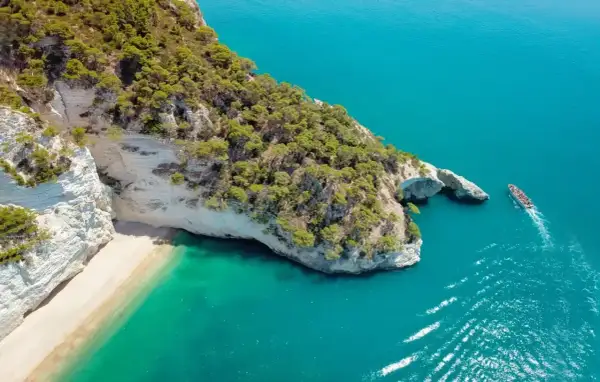 Piękna plaża i turkusowe morze, idealne miejsce, by zastanowić się, gdzie do Włoch na wakacje. Statek wycieczkowy zbliża się do skalistego wybrzeża.