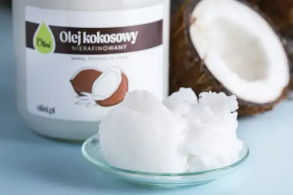Olej kokosowy nierafinowany na talerzyku, obok słoika i połówki kokosa. Idealny do smażenia i pieczenia.