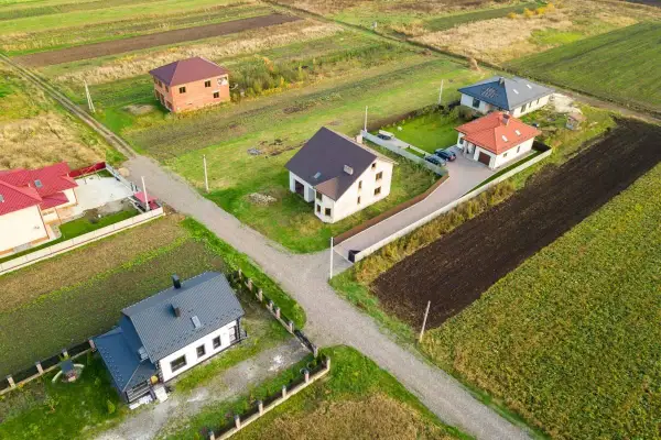 Domy na wsi, zróżnicowana odległość domu od plotu, otoczone polami i zielenią.