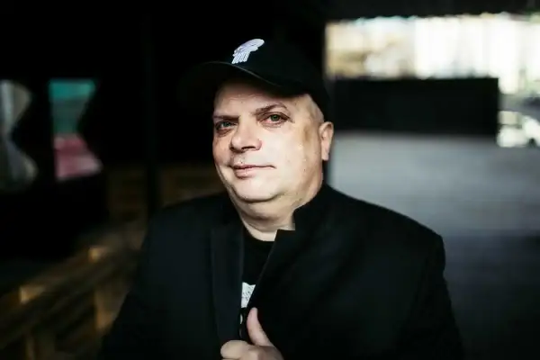 Krzysztof Skiba w czapce z daszkiem i czarnej marynarce, jakby przygotowywał się do wykonania swoich kultowych utworów.