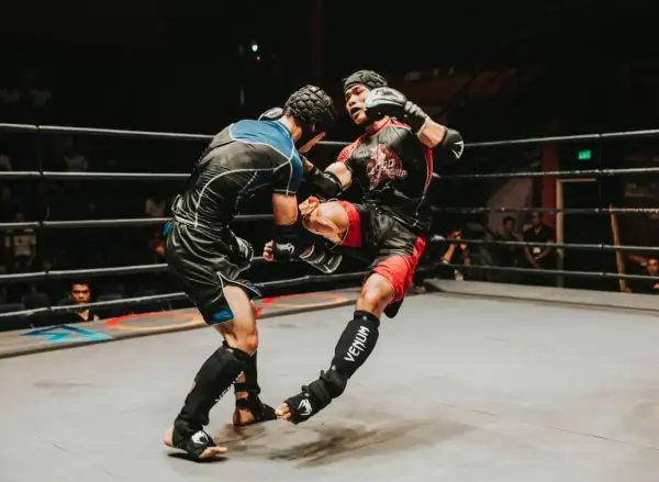 Two fighters in a ring, one delivering a powerful kick. The intensity of the moment showcases the mental fortitude and boxing psychology required for combat sports.