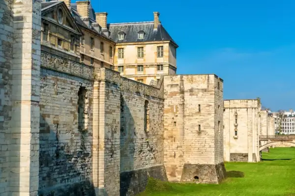 Murs imposants et tours de pierre du **château de Vincennes** sous un ciel bleu éclatant, avec des bâtiments historiques en arrière-plan.