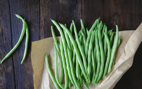 Fagiolini freschi pronti per essere bolliti in acqua fredda o calda, disposti su carta da forno su un tavolo di legno scuro.