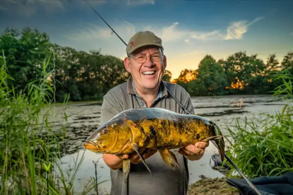 Glücklicher Angler hält großen Fisch am Lohheider See im Abendlicht.