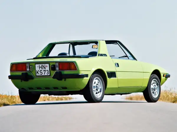 Jasnozielony Fiat X1/9 z lat 70. na pustej drodze, z widokiem na tył i bok.