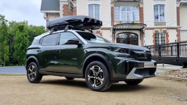 Nowy C3 Aircross w ciemnozielonym kolorze z czarnym boxem dachowym przed eleganckim budynkiem.