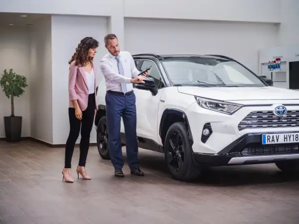 Sprzedawca pokazuje klientce detale białej Toyoty RAV4 na tablecie. To pewne auto dla wymagających.