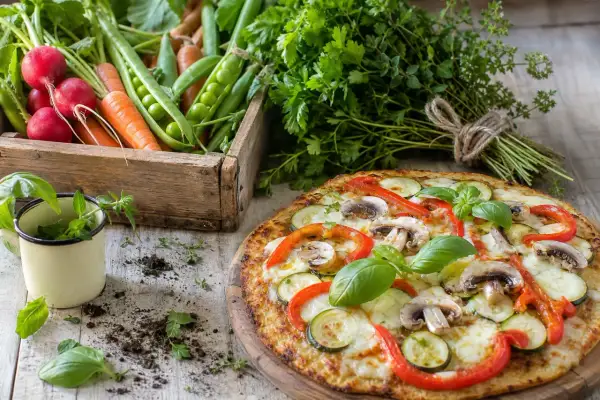 Délicieuse pizza chou fleur garnie de légumes frais, avec une caisse de radis, carottes et petits pois en arrière-plan.