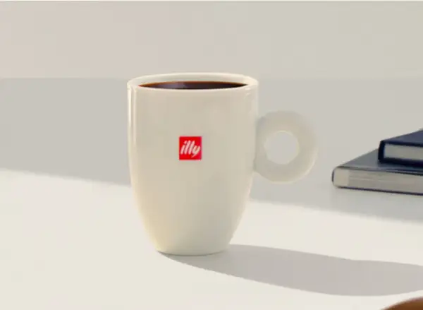 Tazza bianca con logo Illy, piena di caffè americano, pronta per una pausa studio a casa.
