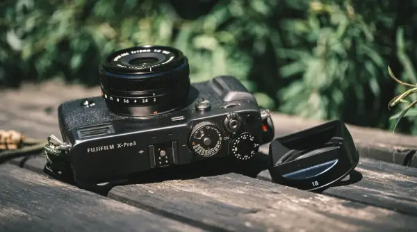 A Fujifilm X-Pro3 camera with a lens and lens hood rests on a wooden surface, ready for a photography review.