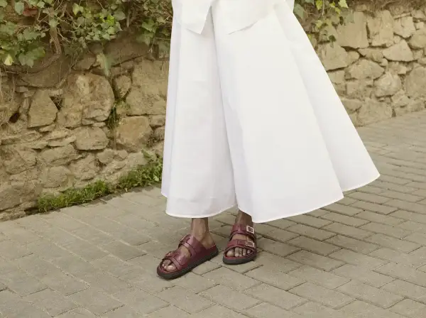 Czerwone sandałki na płaskiej podeszwie idealnie pasują do zwiewnej, białej sukienki. Oto inspiracja, jakie buty do eleganckiej sukienki wybrać na co dzień.