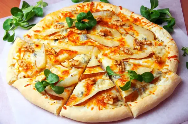 Pyszna pizza z gruszką i serem pleśniowym, posypana orzechami włoskimi i udekorowana świeżą rukolą.