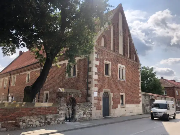 Stary ceglany budynek z kamiennymi detalami, otoczony murem i drzewem. To jedna z kazimierza wielka atrakcji, gdzie historia spotyka się z teraźniejszością.