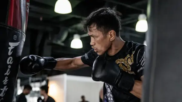 A boxer practices his form, throwing a punch at a heavy bag. His focus is intense as he trains.