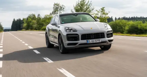 Srebrny Porsche Cayenne 2025 sunie po asfaltowej drodze, otoczony zielenią lasów.