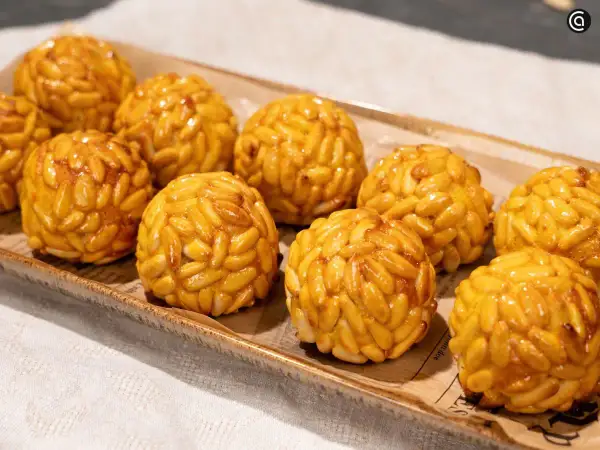 Panellets de boniato cubiertos de piñones dorados, presentados en una bandeja rústica.