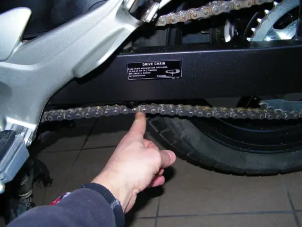 Sprawdzanie naciągu łańcucha w motocyklu. Palec pokazuje luźny łańcuch napędowy.