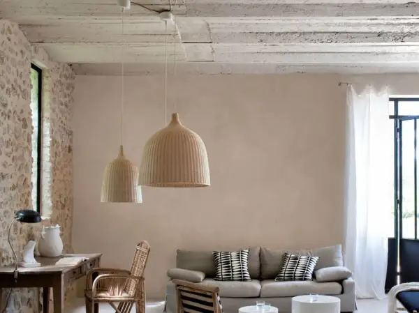Un salon lumineux avec un mur en enduit mur interieur texturé, des suspensions en rotin, un canapé et des meubles en bois.