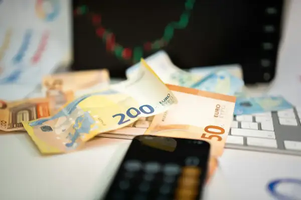 Euro banknoty na klawiaturze, telefon i wykres giełdowy sugerują inwestowanie w waluty.
