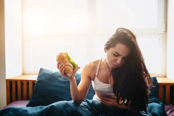 Donna con mal di stomaco tiene un panino, pensando cosa mangiare dopo aver vomitato.