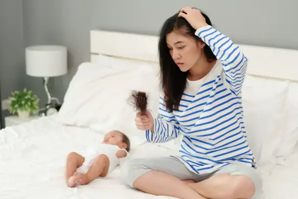 Maman inquiète par la chute de cheveux post-allaitement, cherchant un traitement naturel. Bébé dort paisiblement à côté.