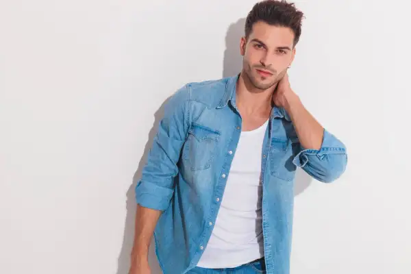 Junger Mann mit lässigem Look: blaues Jeanshemd über einem weißen Unterhemd unter T-Shirt.