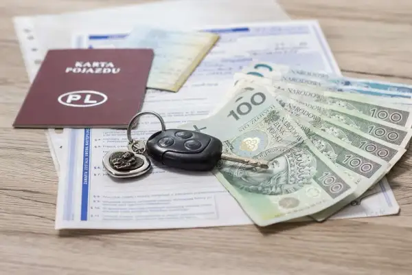 Karta pojazdu, kluczyki i polskie banknoty 100 zł leżą na dokumentach.