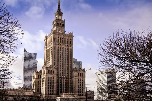 Kulturpalatset Warszawa reser sig stolt mot en molnig himmel, omgiven av moderna skyskrapor och kala trädgrenar.