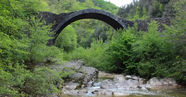 Antico ponte della Pia in pietra, con un arco maestoso, sovrasta un ruscello tra la rigogliosa vegetazione primaverile.